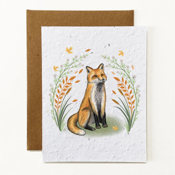 Plantable greeting card with an illustration of a hand drawn fox sitting on his hind legs with front paws stretched in front. He is surrounded by yellow and orange autumn leaves and foliage.