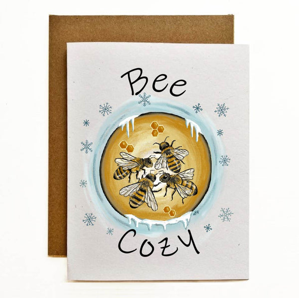 Greeting card featuring a cozy winter-themed design of bees nestled in their hive to stay warm, with the text 'Bee Cozy.' Printed on 100% recycled cardstock.